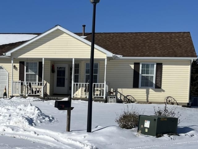 snow covered rear of property featuring a garage and covered porch