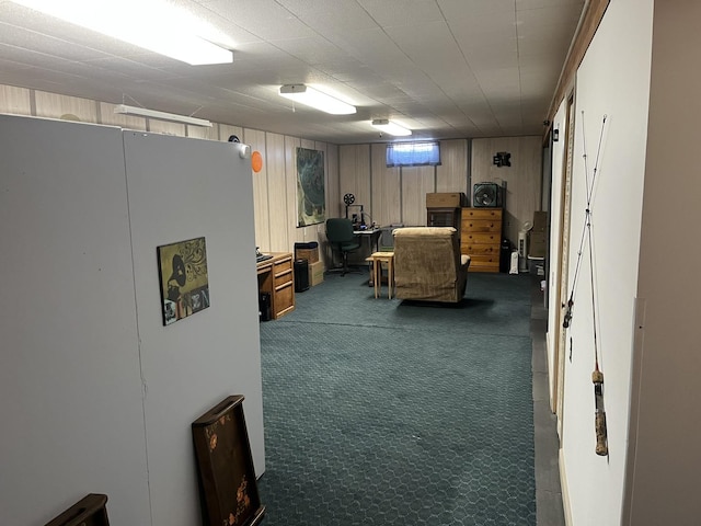 basement featuring white fridge, carpet, and wood walls