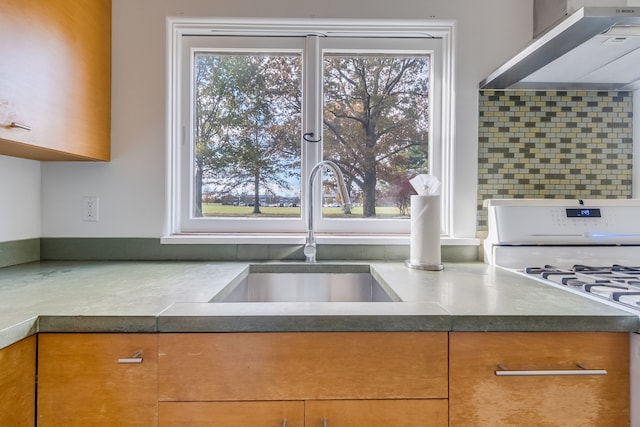 kitchen with backsplash, wall chimney exhaust hood, sink, and white range with gas cooktop