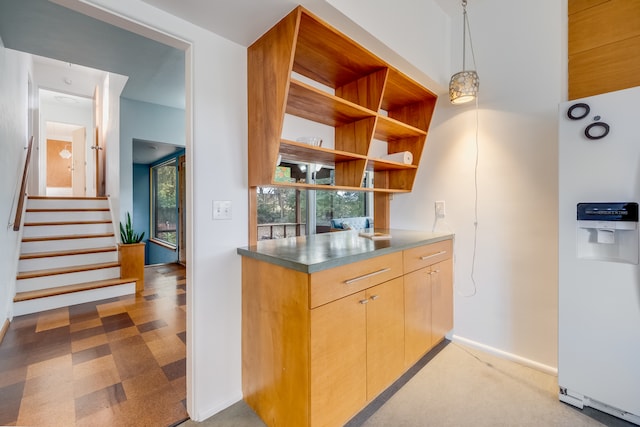 kitchen with stainless steel counters, light brown cabinets, white refrigerator with ice dispenser, decorative light fixtures, and light carpet