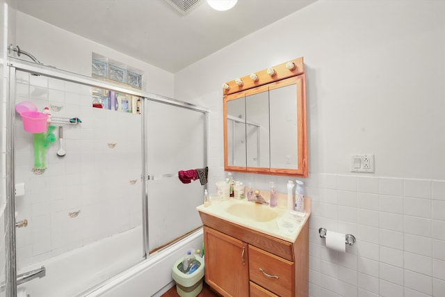 bathroom with tile walls, vanity, and combined bath / shower with glass door