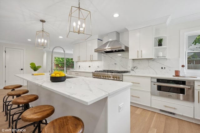 kitchen with pendant lighting, a center island, white cabinets, wall chimney exhaust hood, and appliances with stainless steel finishes