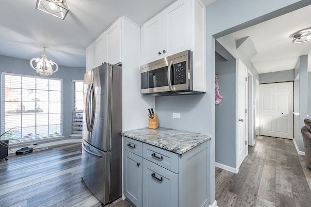 kitchen with dark hardwood / wood-style floors, stainless steel appliances, light stone countertops, a chandelier, and white cabinets