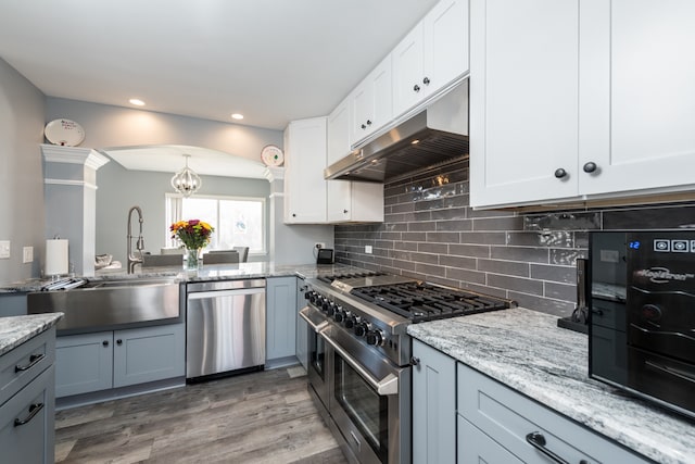 kitchen with white cabinets, backsplash, appliances with stainless steel finishes, hardwood / wood-style flooring, and light stone counters