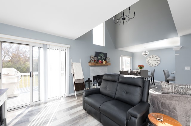 living room featuring a notable chandelier, a towering ceiling, a brick fireplace, and light wood-type flooring