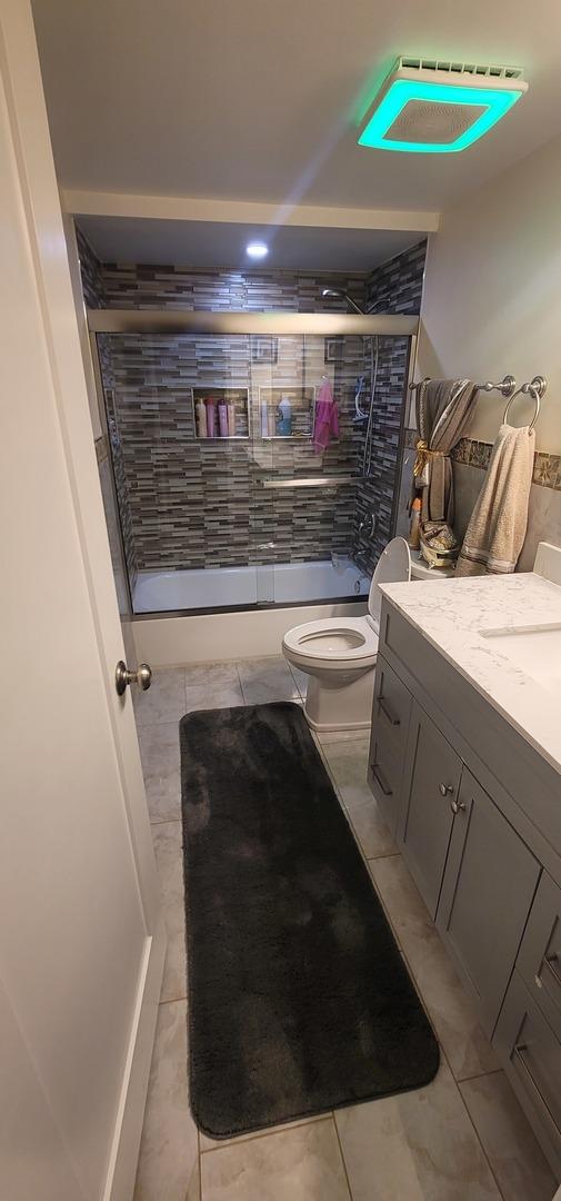 full bathroom with tile patterned flooring, vanity, enclosed tub / shower combo, and toilet