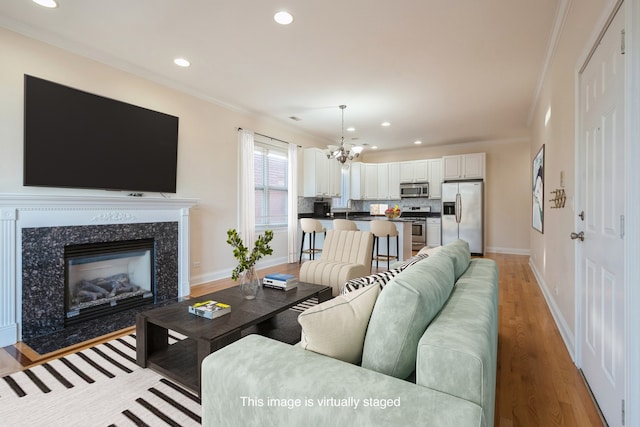 living room featuring sink, a chandelier, crown molding, a high end fireplace, and light wood-type flooring