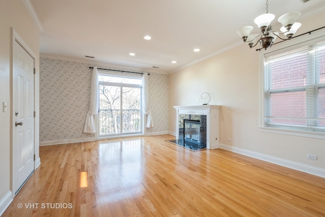 unfurnished living room with an inviting chandelier, a tile fireplace, ornamental molding, and light hardwood / wood-style flooring