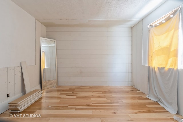 spare room featuring wooden walls, a textured ceiling, and light wood-type flooring