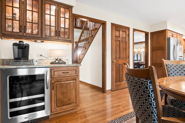 bar with stainless steel appliances, light stone countertops, a chandelier, and light wood-type flooring