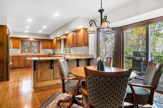 kitchen featuring stainless steel fridge, light stone countertops, light wood-type flooring, pendant lighting, and sink