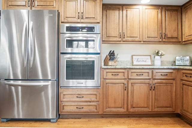 kitchen featuring light stone countertops, appliances with stainless steel finishes, and light hardwood / wood-style flooring