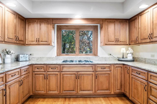 kitchen featuring light stone counters, a tray ceiling, light hardwood / wood-style flooring, and stainless steel gas stovetop