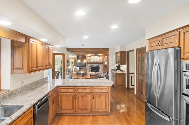 kitchen featuring hanging light fixtures, kitchen peninsula, a brick fireplace, light wood-type flooring, and appliances with stainless steel finishes