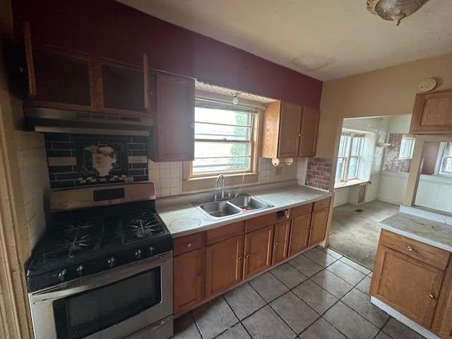 kitchen with light countertops, tasteful backsplash, stainless steel gas range, and a sink