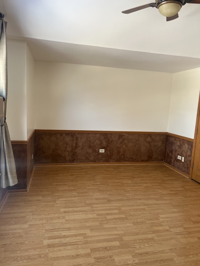 spare room with a wainscoted wall, light wood-style flooring, and a ceiling fan