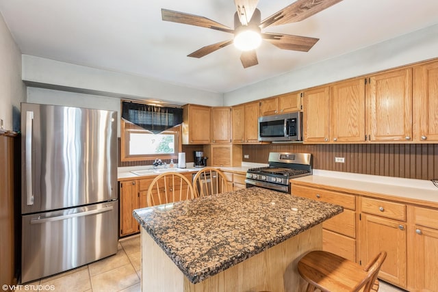 kitchen with a center island, dark stone counters, sink, ceiling fan, and stainless steel appliances