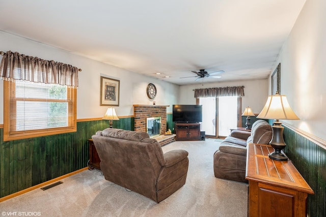 carpeted living area with visible vents, a ceiling fan, a wainscoted wall, wood walls, and a fireplace