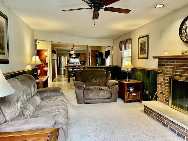 living room featuring light carpet, ceiling fan, wainscoting, and a fireplace