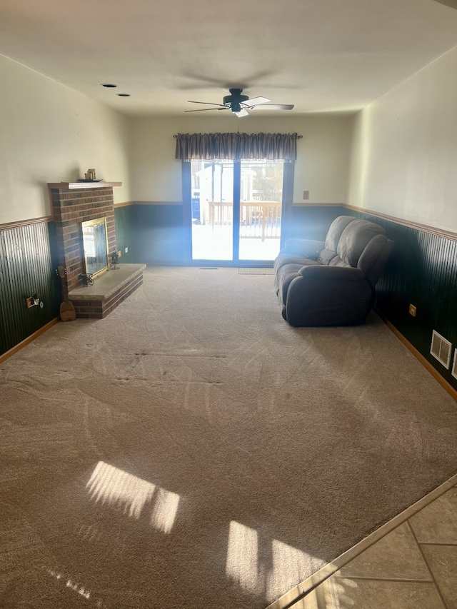 unfurnished living room featuring a ceiling fan, a wainscoted wall, a fireplace, and visible vents