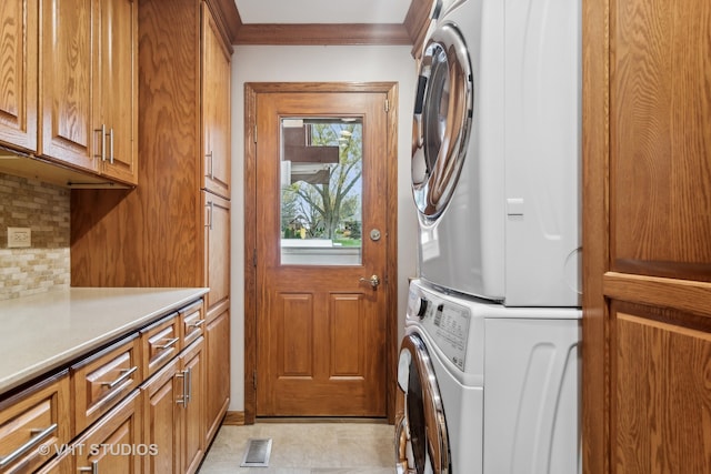 laundry room featuring stacked washer / dryer, light tile patterned flooring, cabinets, and ornamental molding