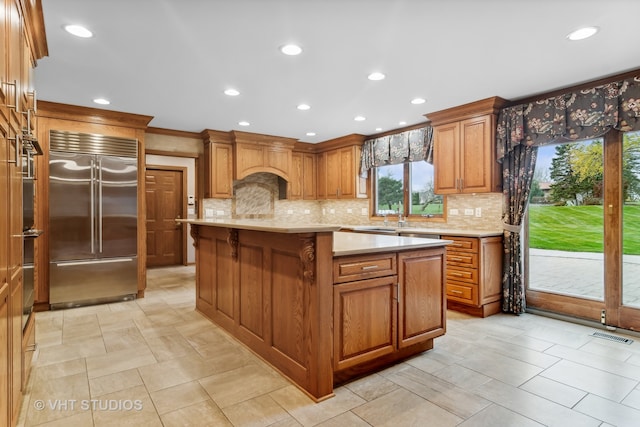 kitchen featuring backsplash, built in refrigerator, a kitchen island, and ornamental molding