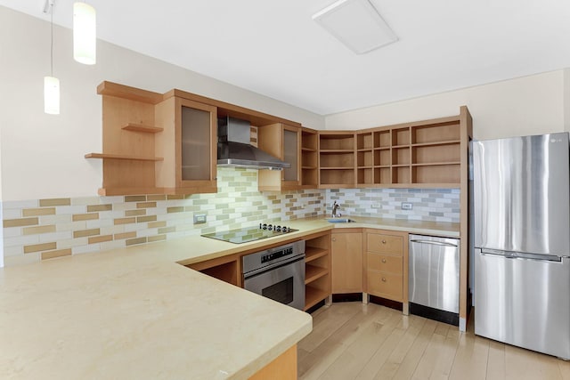 kitchen featuring stainless steel appliances, sink, wall chimney range hood, light hardwood / wood-style flooring, and hanging light fixtures