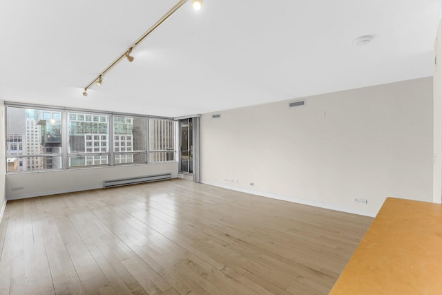 spare room featuring wood-type flooring, track lighting, and a baseboard heating unit