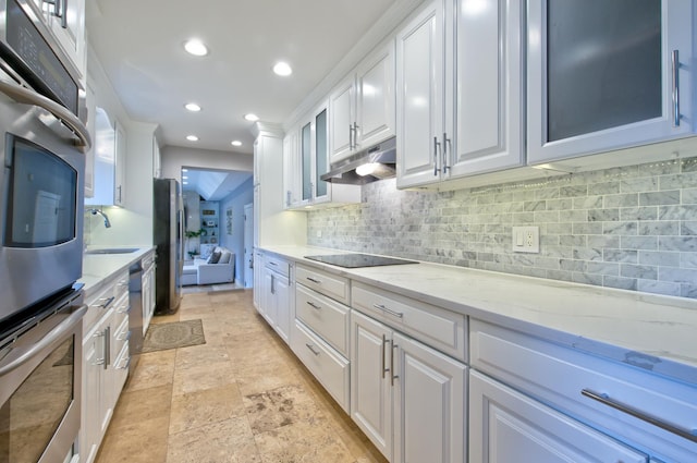 kitchen with sink, tasteful backsplash, light stone counters, appliances with stainless steel finishes, and white cabinets