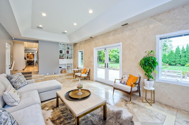 living room featuring a raised ceiling, tile walls, built in features, and french doors