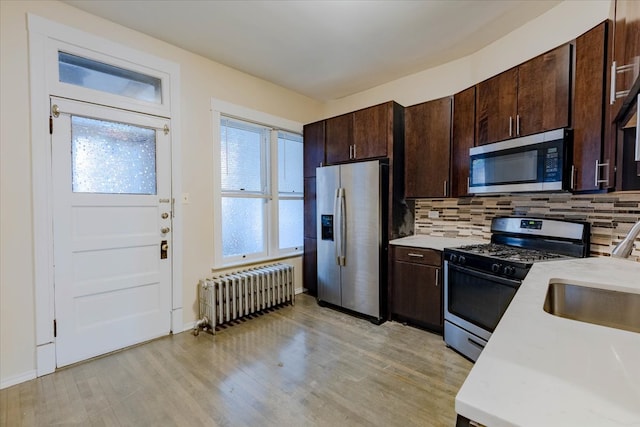 kitchen featuring decorative backsplash, appliances with stainless steel finishes, dark brown cabinets, light hardwood / wood-style flooring, and radiator heating unit