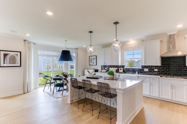 kitchen with a center island, light hardwood / wood-style floors, wall chimney exhaust hood, pendant lighting, and white cabinets