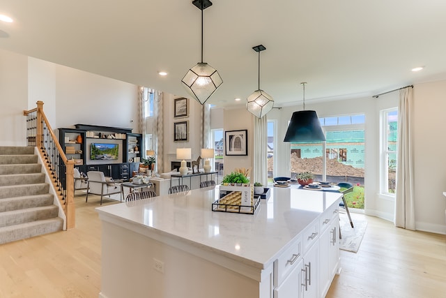 kitchen with white cabinets, hanging light fixtures, light wood-type flooring, a fireplace, and a center island