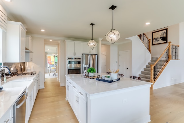 kitchen featuring a kitchen island, stainless steel appliances, pendant lighting, white cabinets, and light hardwood / wood-style flooring