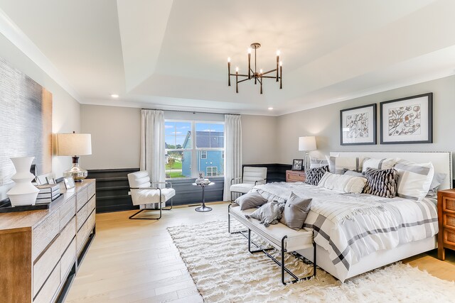 bedroom featuring a tray ceiling, ornamental molding, a chandelier, and light wood-type flooring