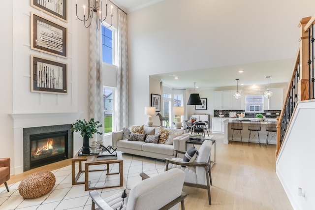 living room featuring a wealth of natural light, an inviting chandelier, a towering ceiling, and light wood-type flooring