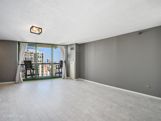 spare room featuring a textured ceiling, light wood-type flooring, and a wall of windows