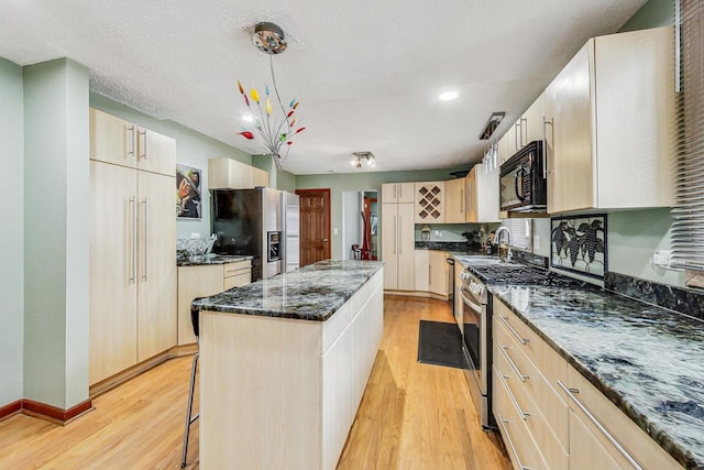 kitchen with a kitchen island, stainless steel appliances, dark stone countertops, pendant lighting, and light wood-type flooring