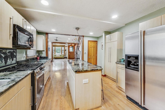 kitchen featuring appliances with stainless steel finishes, light wood-type flooring, a textured ceiling, a center island, and decorative light fixtures