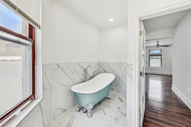 bathroom with tile walls, a bathtub, wood-type flooring, and ceiling fan