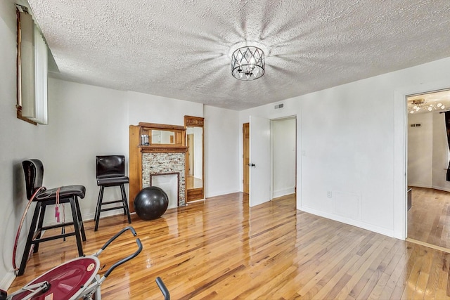 workout room with a textured ceiling, an inviting chandelier, and light wood-type flooring