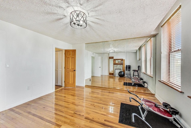 workout room featuring hardwood / wood-style flooring, a textured ceiling, a chandelier, and a stone fireplace