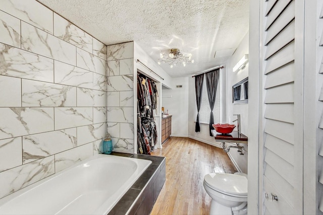 bathroom with tiled bath, a textured ceiling, toilet, and hardwood / wood-style floors