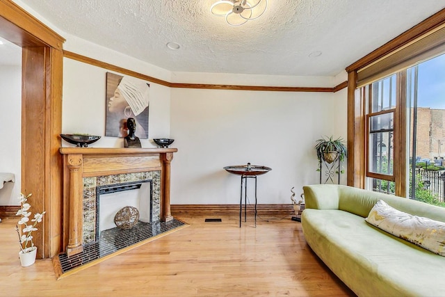 living area featuring crown molding, light hardwood / wood-style flooring, a textured ceiling, and a tile fireplace