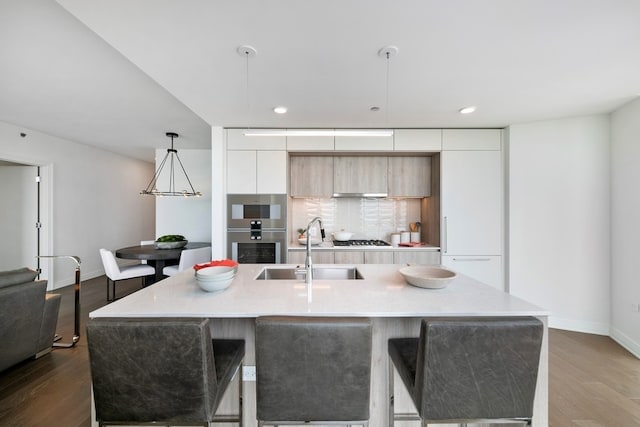 kitchen with hardwood / wood-style flooring, sink, decorative light fixtures, and an island with sink