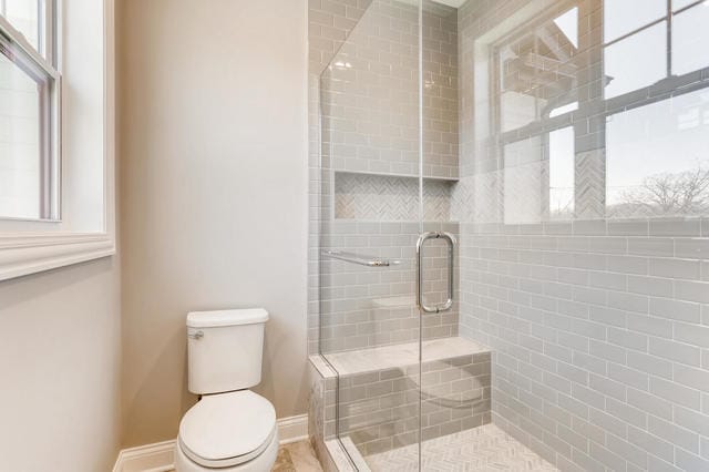 bathroom featuring a healthy amount of sunlight, a shower with shower door, and toilet