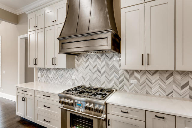 kitchen featuring decorative backsplash, premium range hood, white cabinetry, stainless steel range, and crown molding