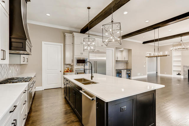 kitchen with custom exhaust hood, beam ceiling, a center island with sink, built in appliances, and decorative light fixtures