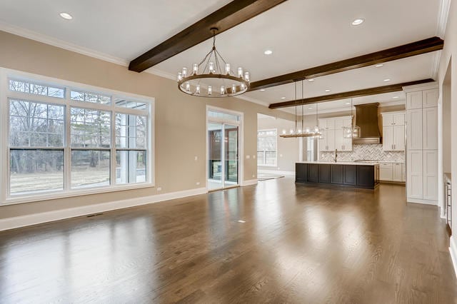 2 Alexandra Dr, Mettawa, IL 60048 - unfurnished living room featuring a chandelier, beamed ceiling, dark wood-type flooring, healthy amount of natural light, and crown molding