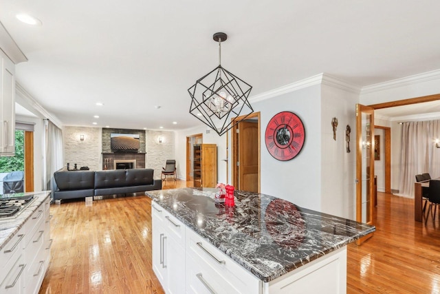 kitchen featuring white cabinets, light hardwood / wood-style floors, a stone fireplace, and crown molding